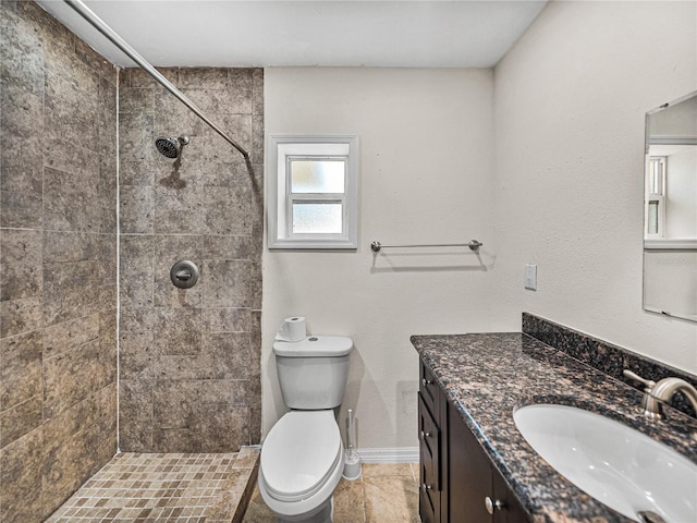 full bathroom featuring a tile shower, vanity, baseboards, and toilet