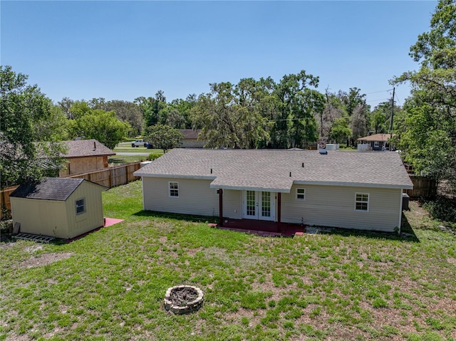 rear view of house with a yard, an outdoor fire pit, fence, a storage unit, and french doors