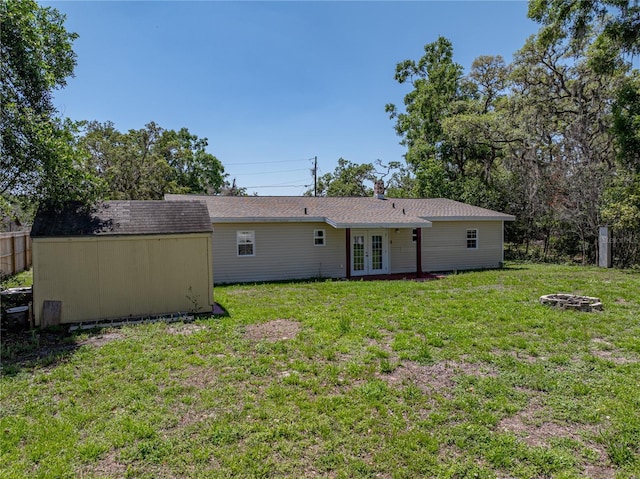 rear view of house with a lawn, fence, an outdoor structure, a storage unit, and french doors