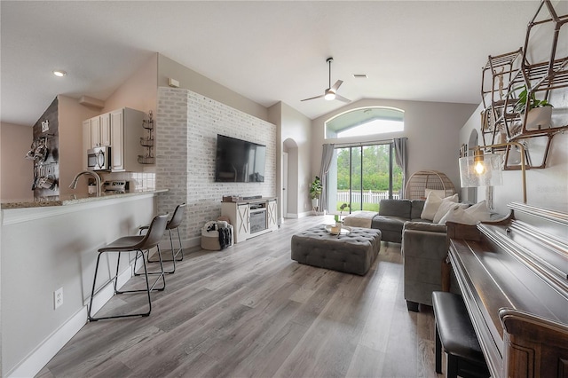 living room featuring baseboards, ceiling fan, arched walkways, light wood finished floors, and vaulted ceiling
