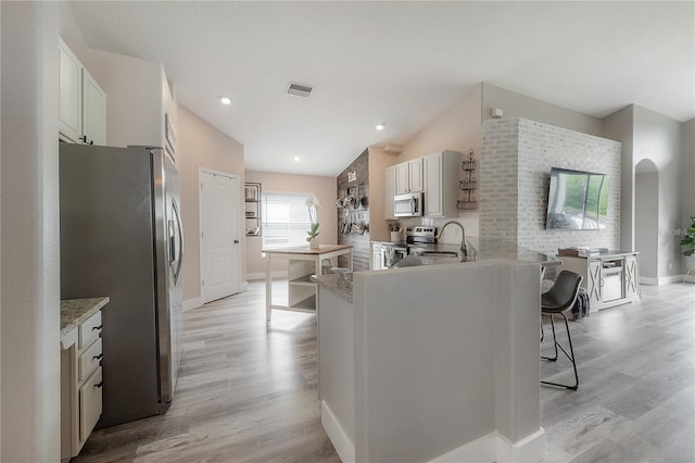 kitchen with visible vents, light wood-type flooring, a sink, a breakfast bar, and stainless steel appliances