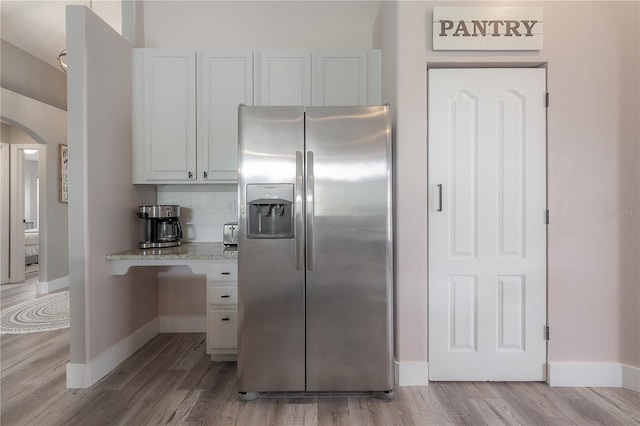 kitchen featuring baseboards, stainless steel refrigerator with ice dispenser, light wood-type flooring, white cabinetry, and arched walkways