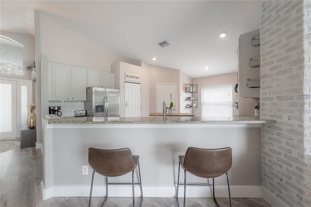 kitchen with stainless steel fridge with ice dispenser, a kitchen breakfast bar, a peninsula, and white cabinets