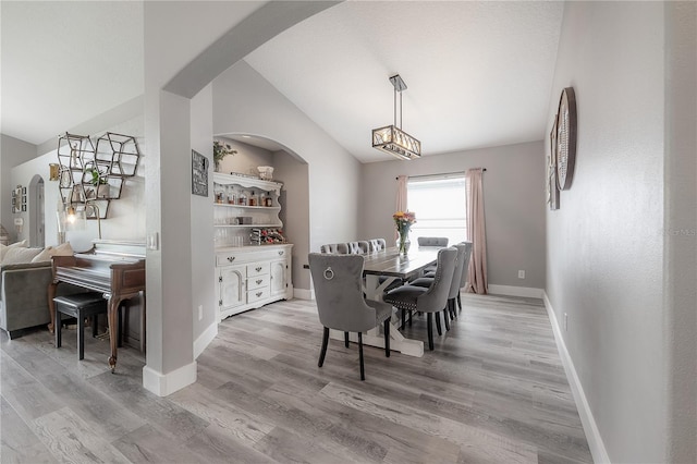dining space featuring arched walkways, baseboards, vaulted ceiling, and light wood-type flooring