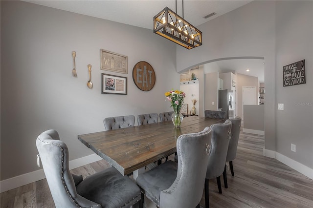 dining space featuring visible vents, arched walkways, wood finished floors, baseboards, and a notable chandelier