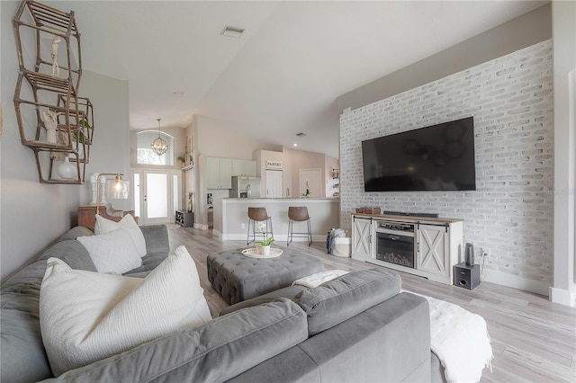 living area featuring visible vents, vaulted ceiling, baseboards, light wood finished floors, and an inviting chandelier