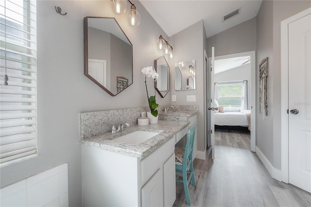 ensuite bathroom featuring a sink, vaulted ceiling, wood finished floors, and visible vents
