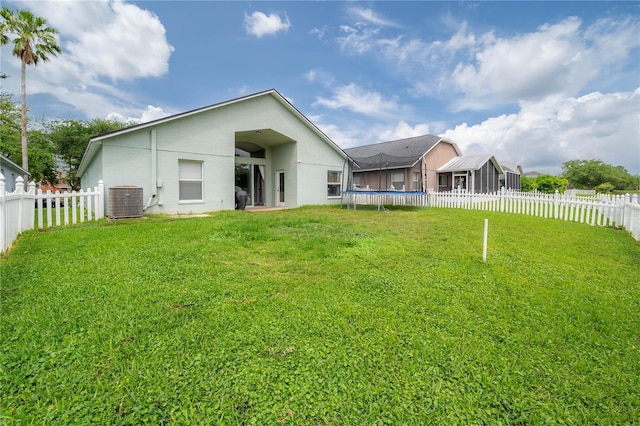 back of property featuring a trampoline, a lawn, central air condition unit, a fenced backyard, and stucco siding