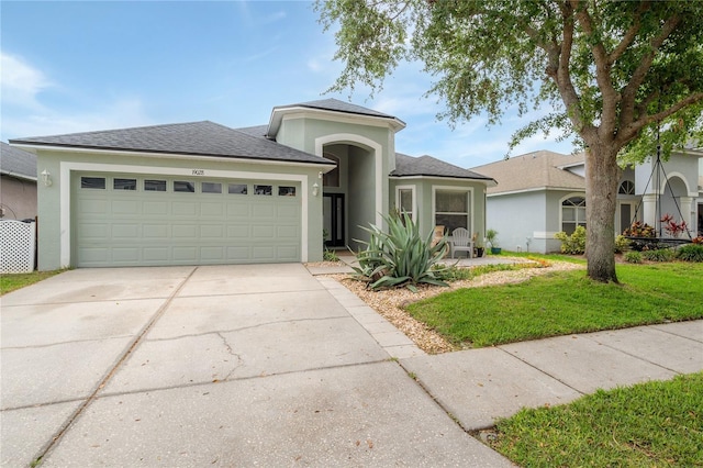 view of front of home featuring roof with shingles, a front yard, concrete driveway, an attached garage, and stucco siding