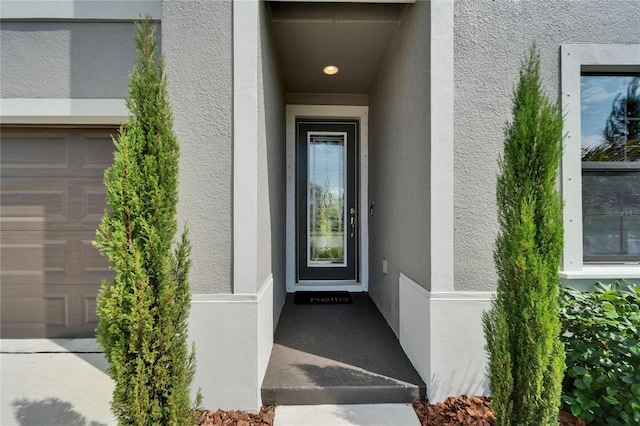 view of exterior entry featuring a garage and stucco siding