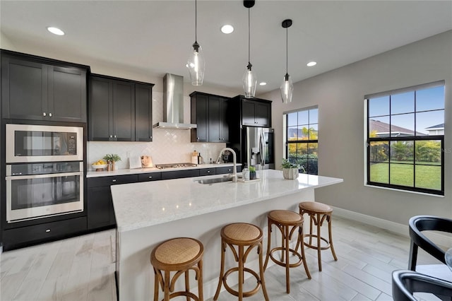 kitchen with dark cabinets, baseboards, wall chimney exhaust hood, stainless steel appliances, and a sink