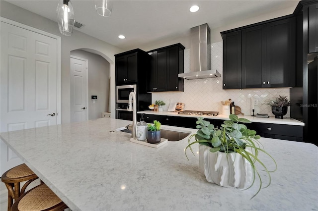 kitchen with dark cabinetry, arched walkways, wall chimney exhaust hood, and stainless steel appliances