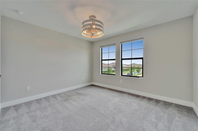 carpeted empty room featuring baseboards and an inviting chandelier