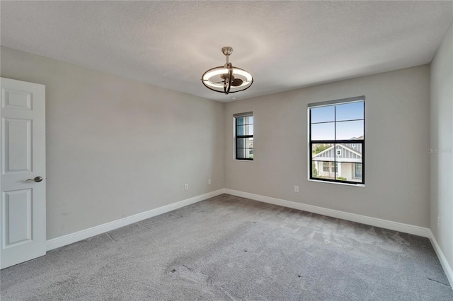 spare room with carpet flooring, baseboards, and an inviting chandelier