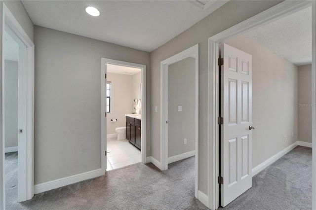 hallway with baseboards and light colored carpet