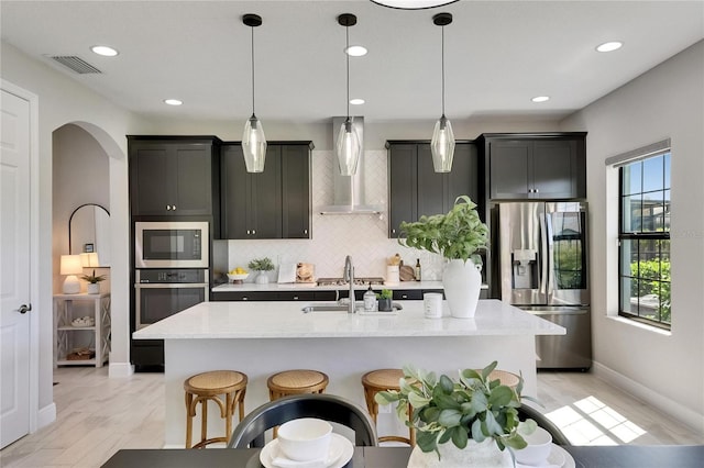 5601 Limelight Dr, Apollo Beach, FL 33572 - kitchen with appliances with stainless steel finishes, wall chimney range hood, arched walkways, tasteful backsplash, and an island with sink