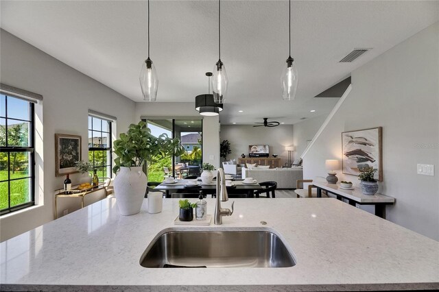5601 Limelight Dr, Apollo Beach, FL 33572 - kitchen with open floor plan, light stone counters, a ceiling fan, a kitchen island with sink, and hanging light fixtures