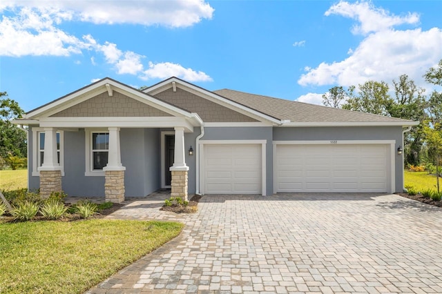 craftsman-style house with a garage, decorative driveway, a front lawn, and stucco siding