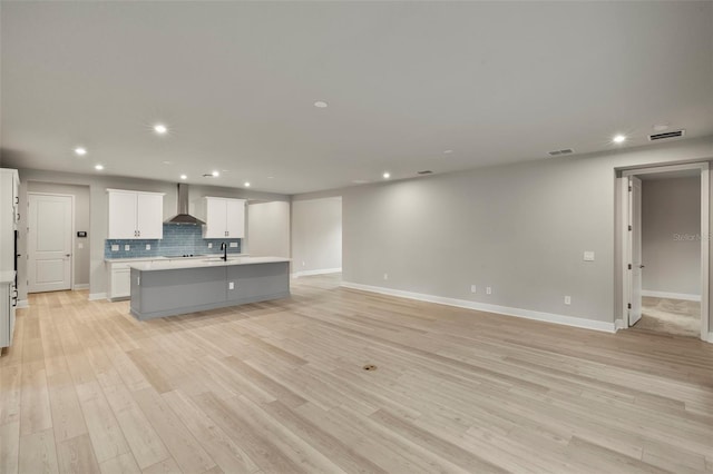 kitchen featuring a center island with sink, light countertops, light wood-style floors, recessed lighting, and wall chimney exhaust hood