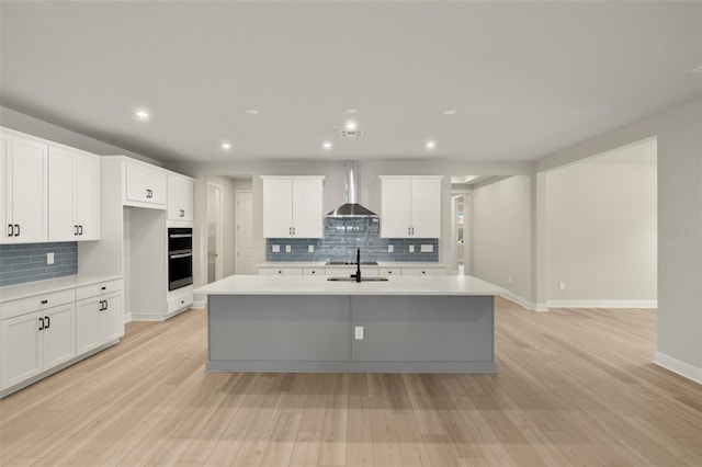 kitchen featuring multiple ovens, decorative backsplash, a sink, and wall chimney exhaust hood