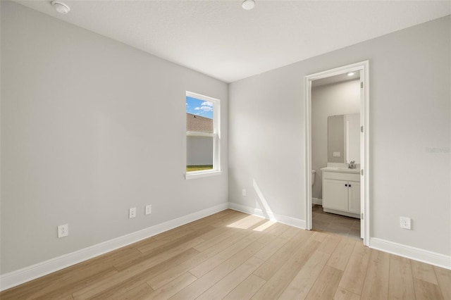 unfurnished bedroom featuring light wood-type flooring, baseboards, and ensuite bath