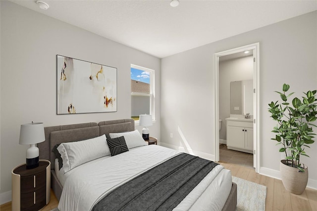bedroom featuring baseboards, ensuite bathroom, and light wood-type flooring
