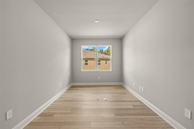 empty room with a textured ceiling, baseboards, and light wood-type flooring