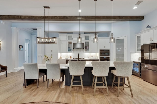 kitchen with light countertops, tasteful backsplash, under cabinet range hood, beamed ceiling, and visible vents