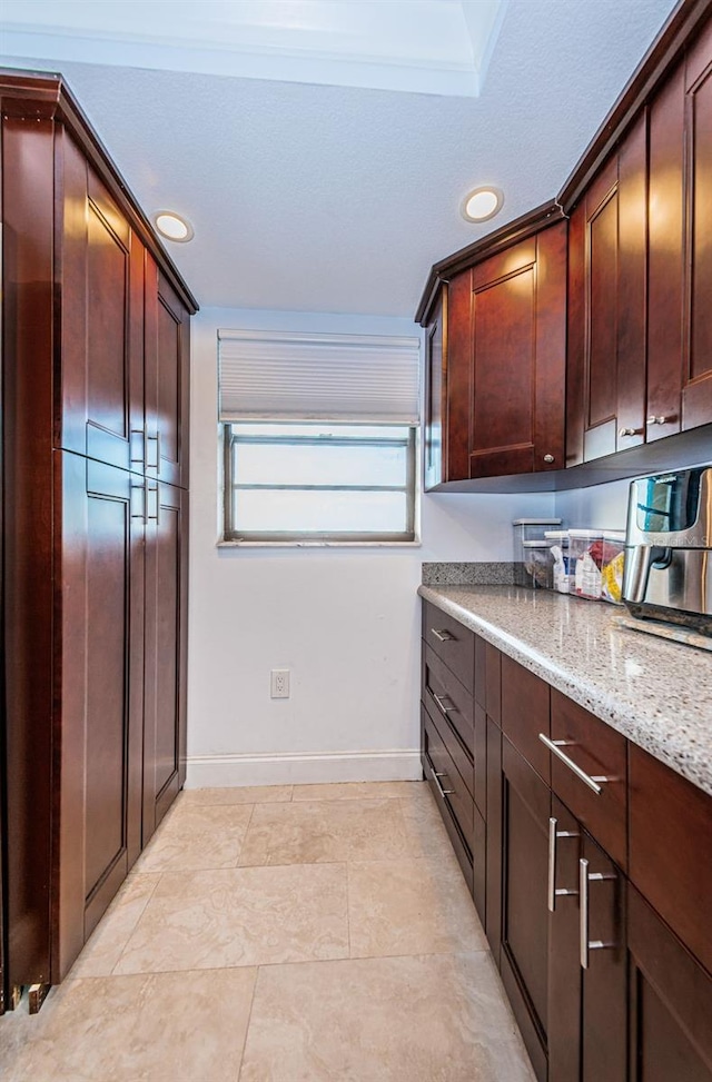 kitchen featuring recessed lighting, baseboards, light stone countertops, and dark brown cabinetry