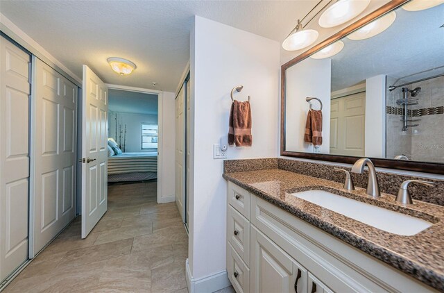 bathroom featuring a textured ceiling, tiled shower, vanity, ensuite bath, and baseboards