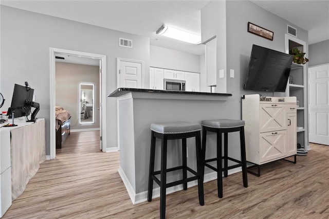 kitchen with stainless steel microwave, light wood-style flooring, visible vents, and a breakfast bar
