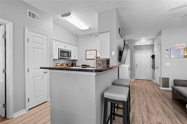 kitchen with dark countertops, a kitchen breakfast bar, white cabinets, stainless steel microwave, and visible vents