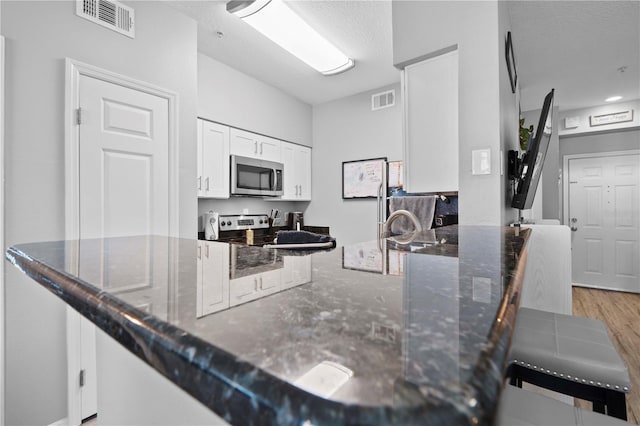 kitchen with visible vents, stainless steel appliances, and dark stone countertops