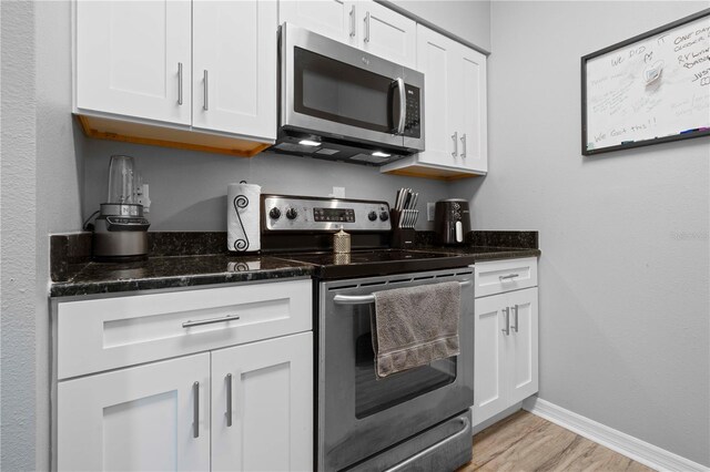 kitchen with dark stone counters, baseboards, light wood-style floors, white cabinetry, and appliances with stainless steel finishes