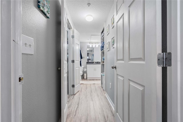 hall with a textured wall, a textured ceiling, and light wood-style flooring