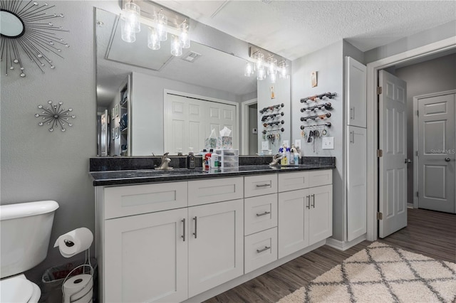bathroom with double vanity, wood finished floors, toilet, a sink, and a textured ceiling