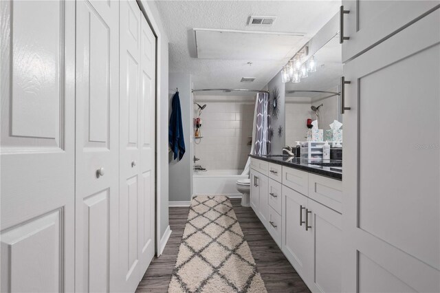 bathroom featuring visible vents, toilet, vanity, shower / bath combo with shower curtain, and a textured ceiling