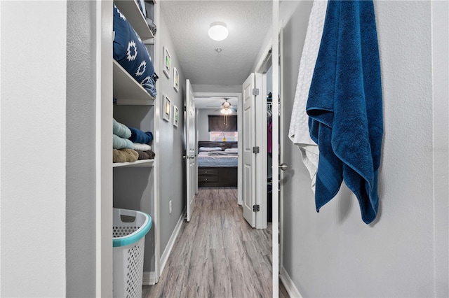 hall with baseboards, wood finished floors, and a textured ceiling