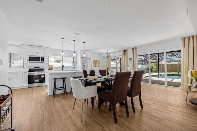 12641 98th St, Largo, FL 33773 - dining area with a textured ceiling, light wood finished floors, a notable chandelier, and a healthy amount of sunlight