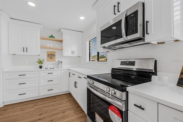 12641 98th St, Largo, FL 33773 - kitchen featuring light wood-type flooring, open shelves, white cabinets, light stone countertops, and appliances with stainless steel finishes