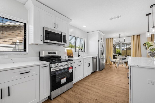 12641 98th St, Largo, FL 33773 - kitchen with visible vents, a sink, light wood-type flooring, appliances with stainless steel finishes, and white cabinetry