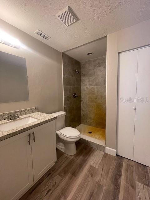 bathroom with tiled shower, visible vents, toilet, and wood finished floors