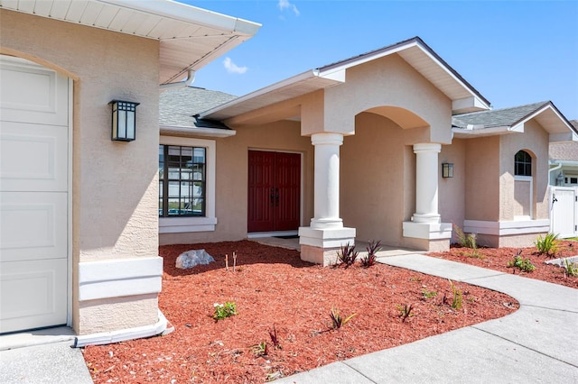 entrance to property featuring a garage, roof with shingles, and stucco siding
