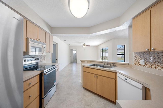 kitchen with ceiling fan, a peninsula, appliances with stainless steel finishes, a sink, and backsplash