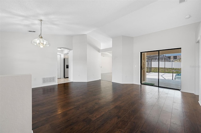 unfurnished room with visible vents, arched walkways, vaulted ceiling, and hardwood / wood-style flooring