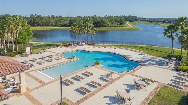 community pool with a patio, fence, and a water view