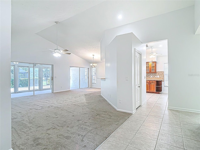 unfurnished living room with light tile patterned floors, baseboards, ceiling fan with notable chandelier, high vaulted ceiling, and light carpet