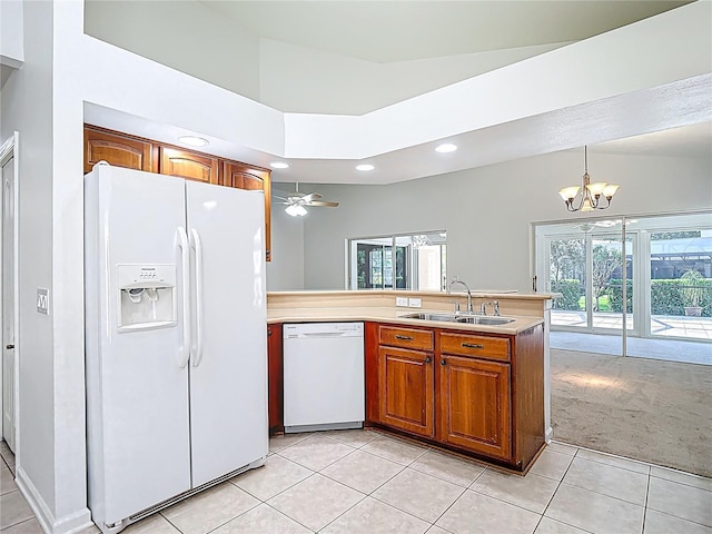 kitchen with light tile patterned floors, white appliances, a peninsula, a sink, and brown cabinets