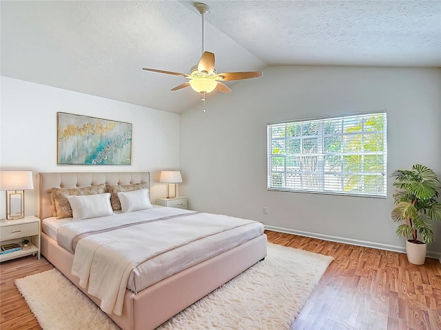 bedroom featuring baseboards, a ceiling fan, a textured ceiling, wood finished floors, and lofted ceiling