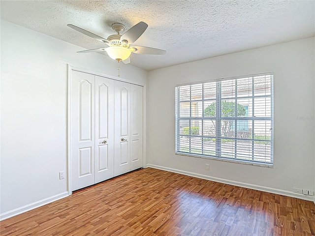 unfurnished bedroom featuring a closet, baseboards, a textured ceiling, and wood finished floors